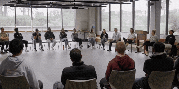 Student with backpack working at a desk, facing glowing digital visuals and screens.