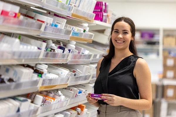 Photo: a pharmacist standing in a dispensary holding a box of medication