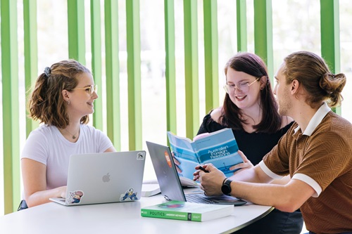 Photo: three Bachelor of Arts students browsing politics text books at a table